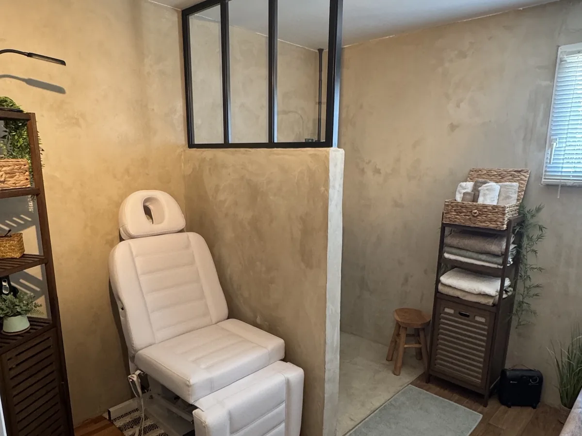La même pièce après travaux : douche à l'italienne de plain-pied derrière une cloison à verrière, sol carrelé imitation bois